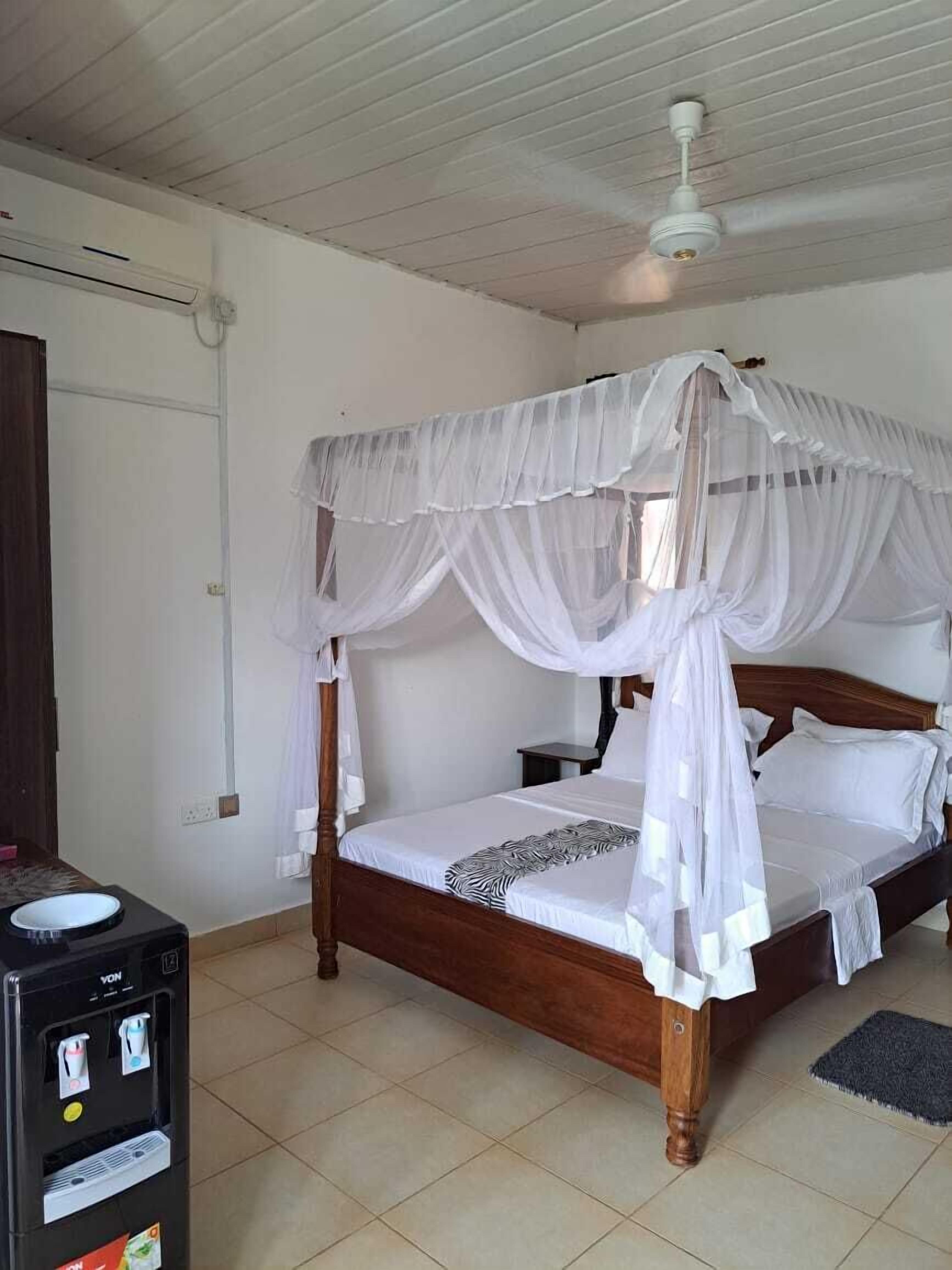 A four-poster bed with a canopy, a water dispenser, and a tiled floor.