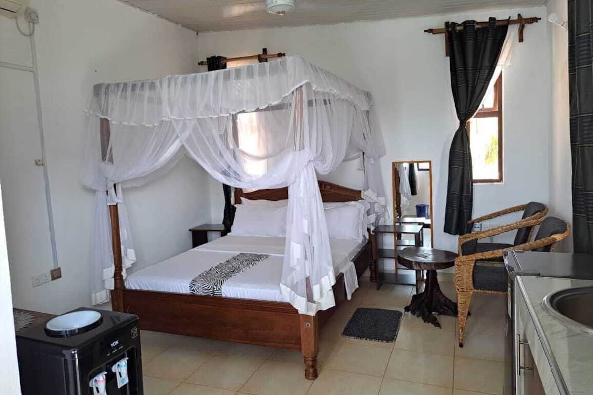 A room with a bed, a small table, a chair, a mirror, and a sink.