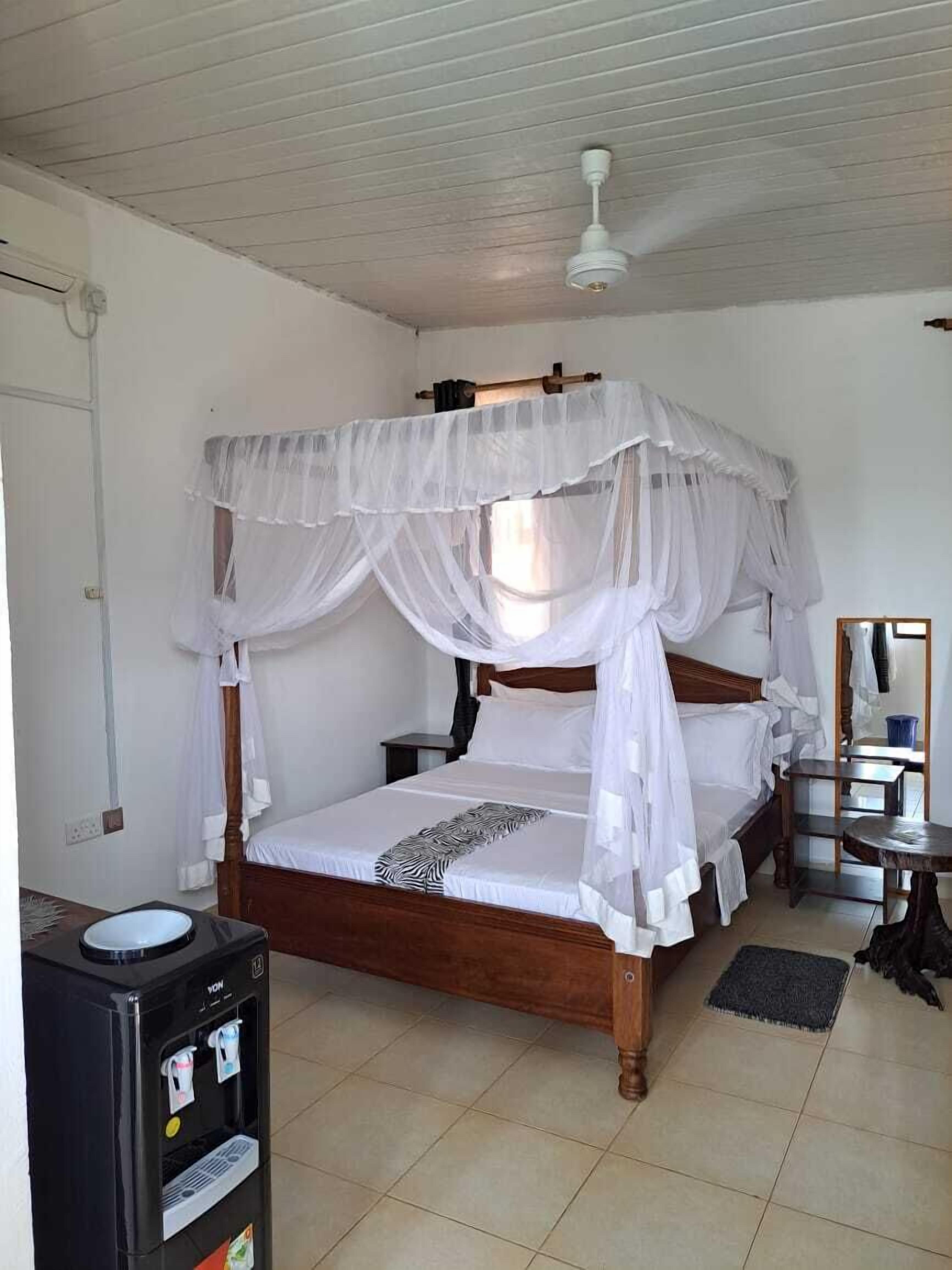 A single bed with a canopy, a water dispenser, a mirror, and a small table.
