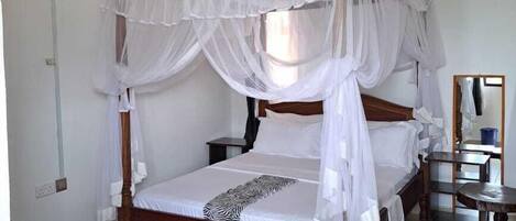 A single bed with a canopy, a water dispenser, a mirror, and a small table.