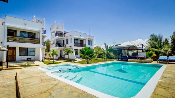 A modern hotel with a swimming pool, multiple balconies, and a well-maintained garden. - Taraji Suites Diani (Diani Beach)