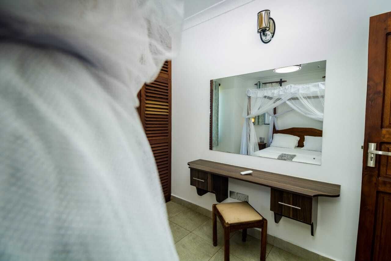 Quarto com cama, mesa de cabeceira, espelho e porta de madeira.