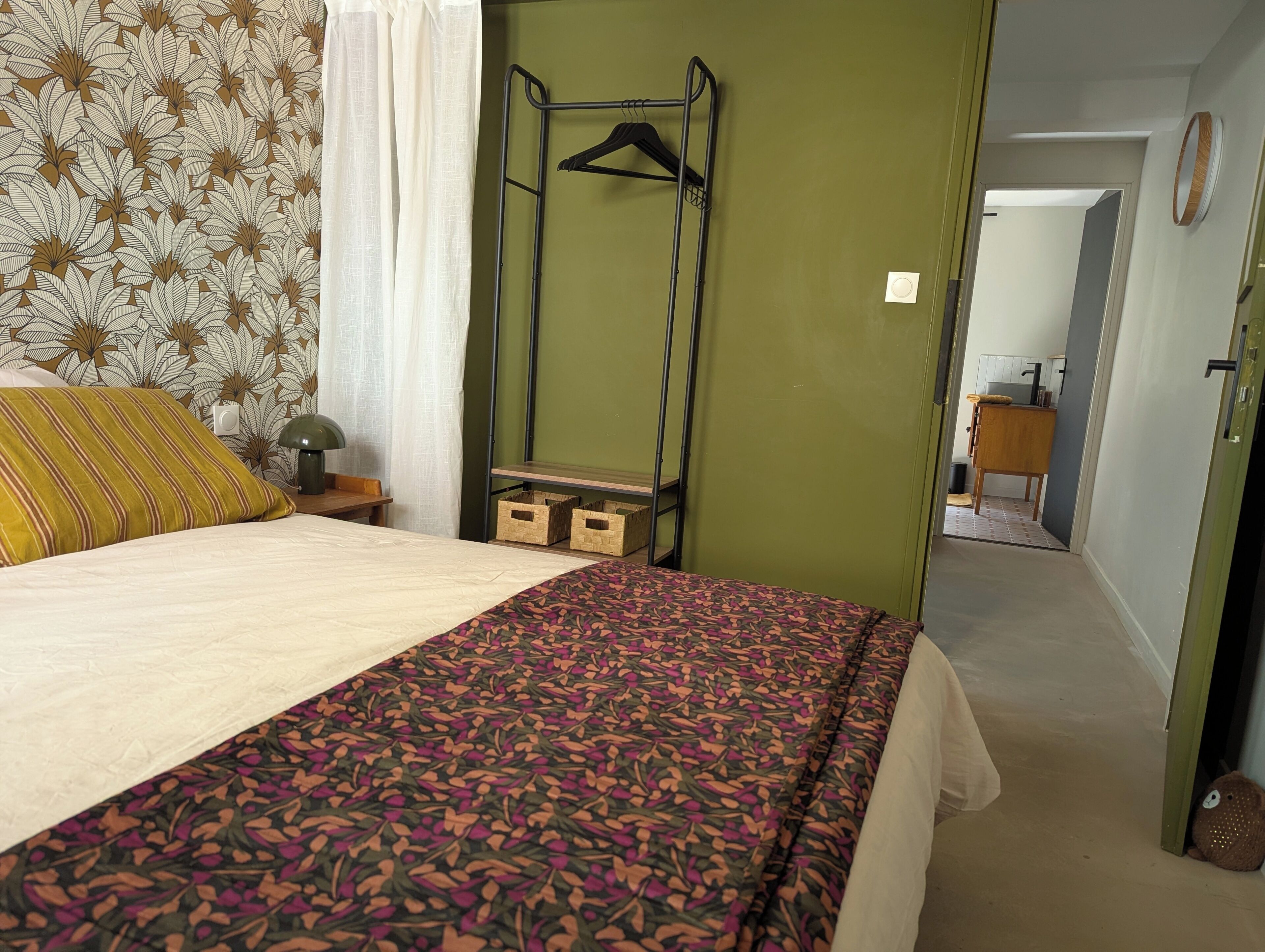 A bedroom with a bed, a bedside table with a lamp, a hanging clothes rack, and a green wall.