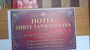 A hotel reception desk with a sign for Hotel Shree Sanwaliya Inn, including check-in and check-out times, and contact information for the hotel. - Hotel Shree Sanwaliya Inn (Ayodhya)