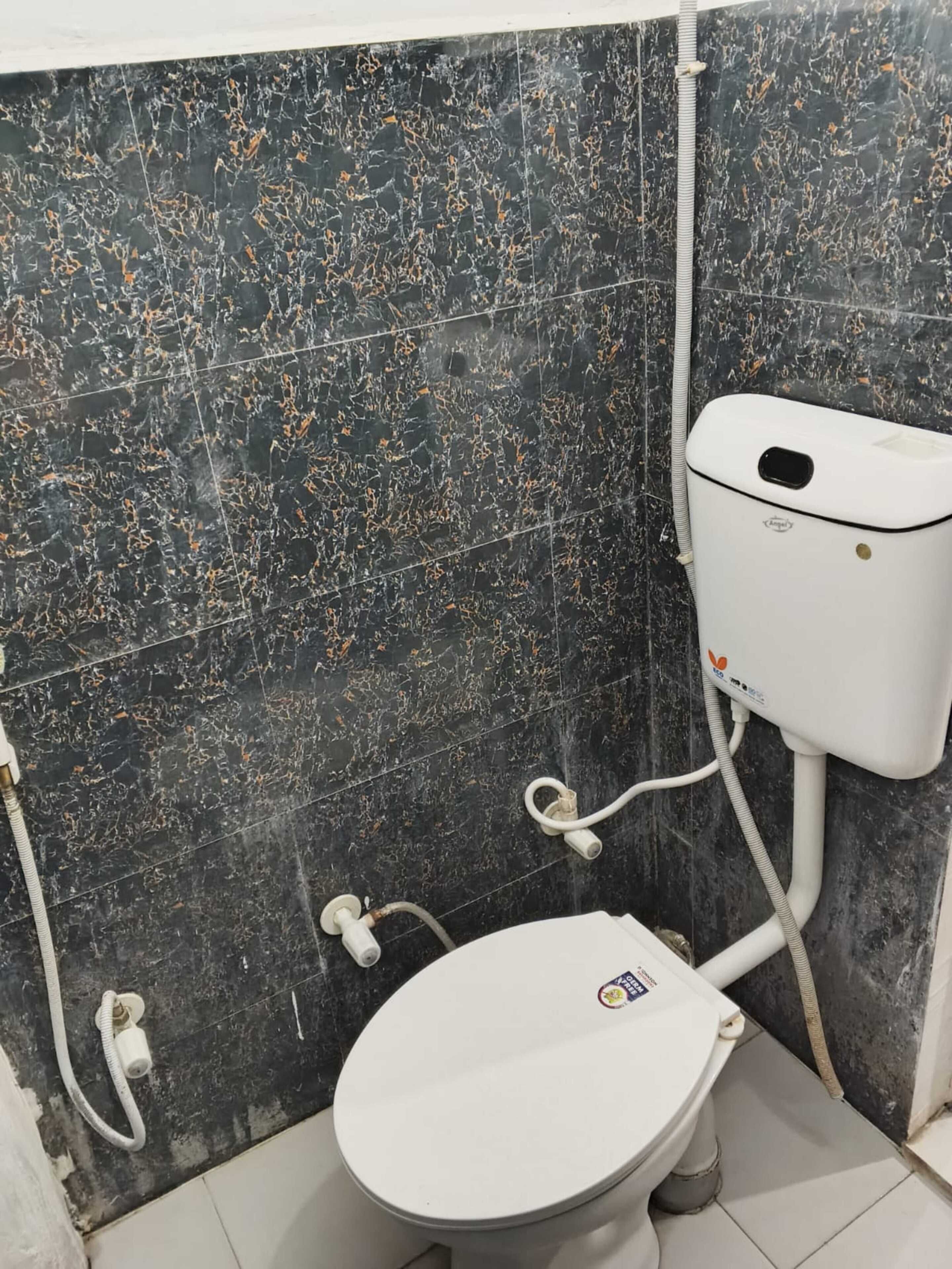 Un baño con inodoro, azulejos de mármol negro y tanque de inodoro blanco.