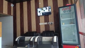 A seating area with a wall-mounted television, a Coca-Cola refrigerator, and a tiled floor. - Hotel Shree Sanwaliya Inn (Ayodhya)