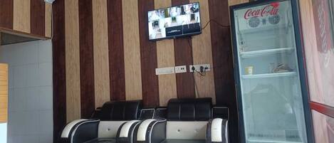 A seating area with a wall-mounted television, a Coca-Cola refrigerator, and a tiled floor.
