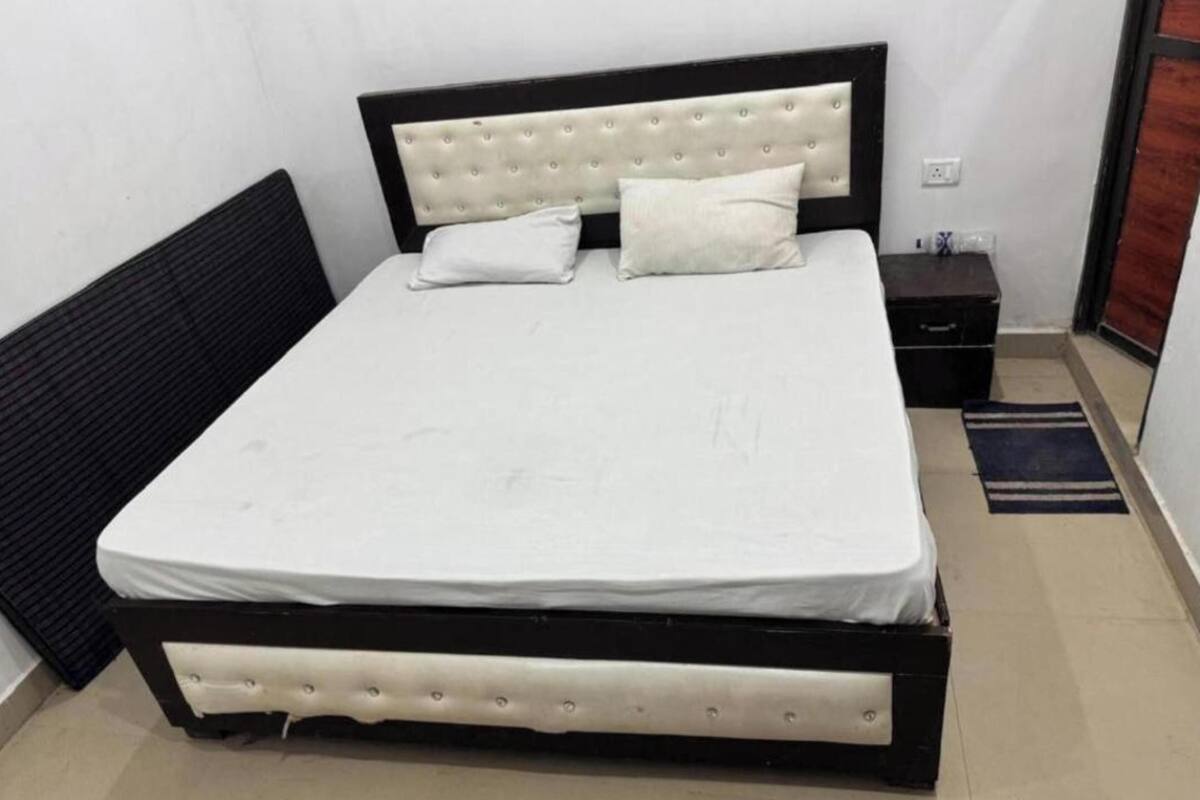 Una cama con estructura negra y cabecera blanca, un colchón blanco y dos almohadas.