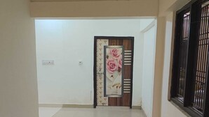 A corridor with a tiled floor, a door with a floral design, and a window with bars. - Hotel Shree Sanwaliya Inn (Ayodhya)