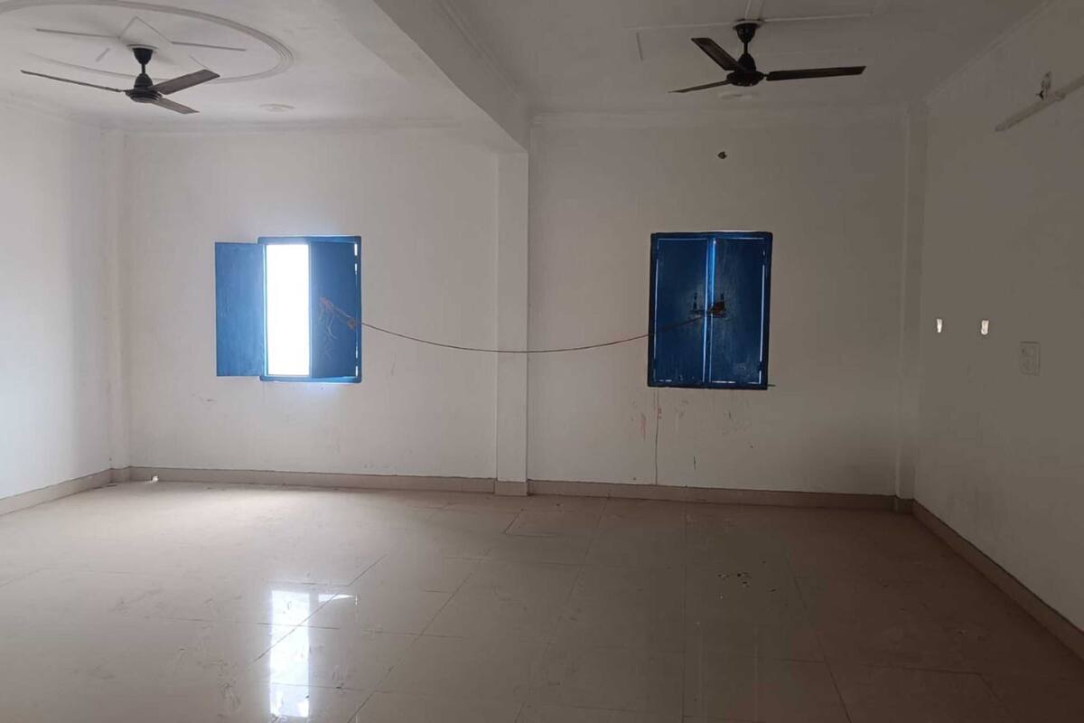 Una habitación amplia con dos ventiladores de techo, suelo de baldosas y dos ventanas con marcos azules.