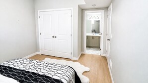 Ein Schlafzimmer mit Bett, einer weißen Tür, einem Badezimmer mit Spiegel und einem Flur.