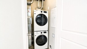 Ein Waschraum mit zwei übereinander gestapelten Samsung Waschmaschinen, einem Warmwasserbereiter und einer weißen Tür.