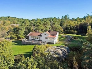 Ein zweistöckiges Haus mit großer Terrasse und Schwimmbecken, umgeben von üppiger Vegetation und Hügeln.