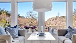 Una habitación con una mesa blanca, dos sofás, un ventanal con vistas a un paisaje rocoso y una lámpara colgante.