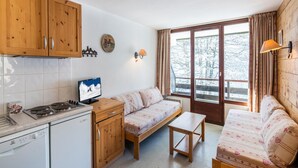 A compact room with a kitchenette, a sofa, a small table, and a window with a view of trees. - Central Alpine Stay for 5 in Morillon (Morillon)