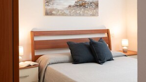 Une chambre à coucher avec un lit en bois, une table de chevet avec une lampe, une autre table de chevet avec un livre ouvert, et un tableau représentant un phare accroché au mur.