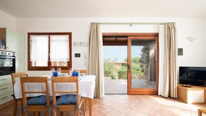 Un coin repas avec une table dressée pour quatre personnes, une cuisine équipée d’un four et une porte-fenêtre coulissante donnant sur une terrasse.