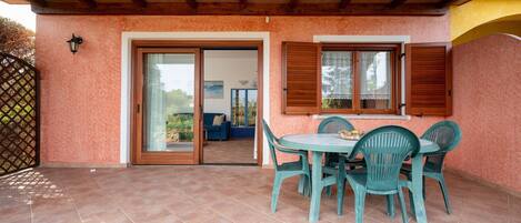 A covered patio with a table and chairs, a sliding glass door, and a view of the outdoors.