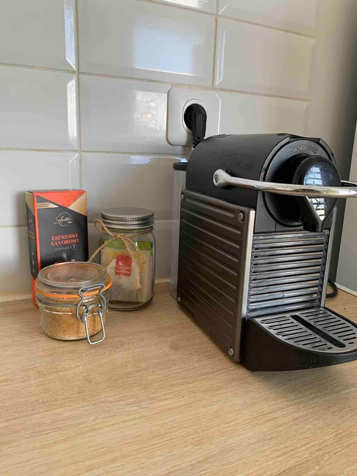 Eine Kaffeemaschine, eine Kaffeeglas und eine Schachtel mit Kaffeekapseln auf einer Küchenarbeitsplatte.