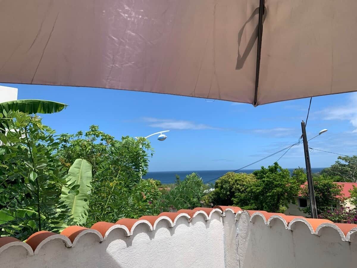 Une vue depuis un balcon doté d’une balustrade blanche, d’un grand parasol et d’un ciel bleu dégagé.