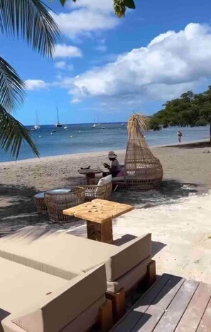 A beachside seating area with wicker furniture and a wooden table, overlooking the sea with boats in the distance. - Ocean bay 1 Nice studio walking distance to the beach (Schœlcher)