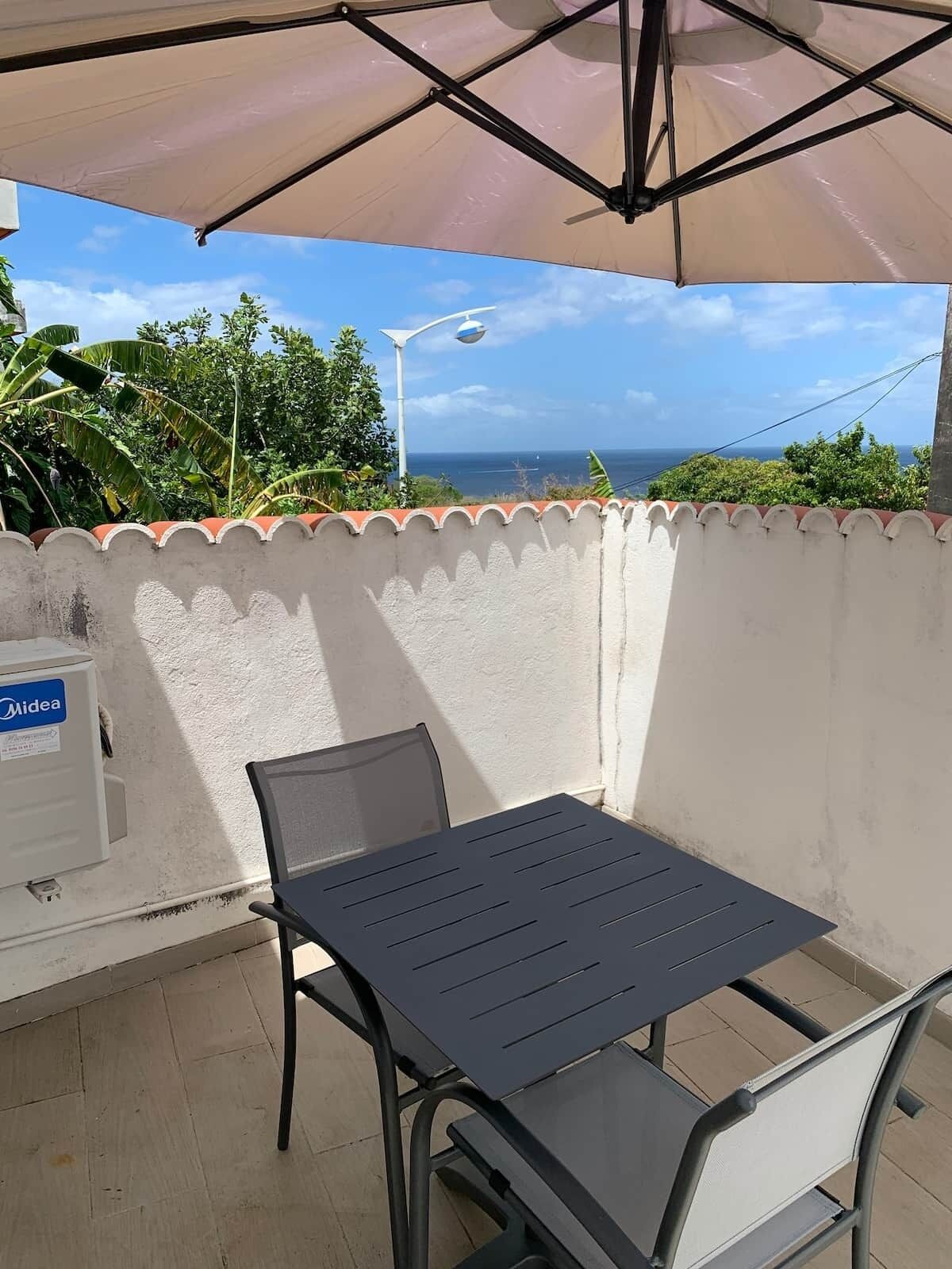 A patio with a table and chairs, a white wall, and a view of the sea.