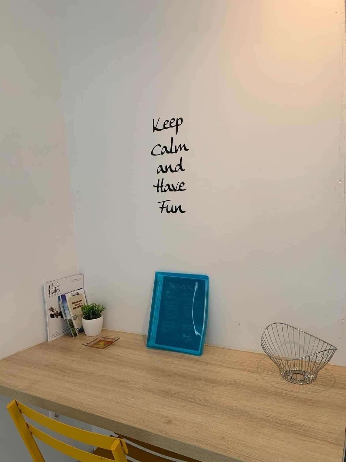 A dining table with a sign saying 'Keep calm and have fun,' a menu stand, a potted plant, and a metal bowl.