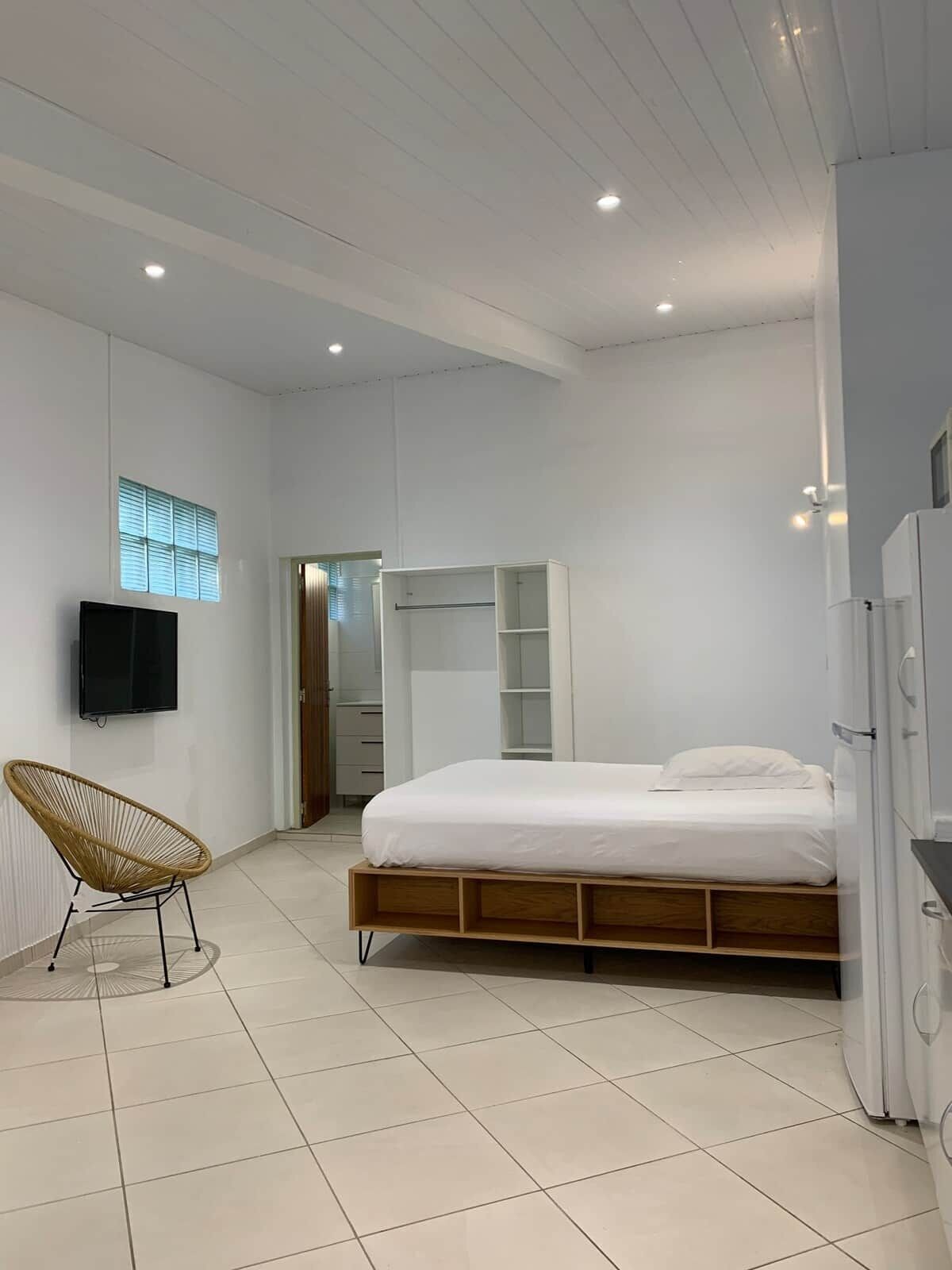 A modern bedroom with a bed, a TV, a chair, and built-in storage.