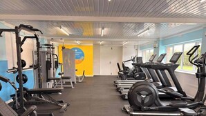 Una palestra con attrezzature per esercizi, un muro con la scritta California e finestre.