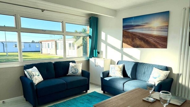 Un soggiorno con due divani blu scuro, un tappeto color verde acqua, un tavolino in legno e un quadro raffigurante una spiaggia.