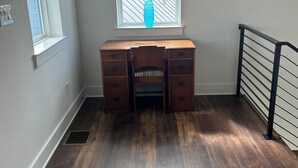 Ein Zimmer mit Schreibtisch aus Holz, einem Fenster mit Jalousien, einer Heizung und einem Metallgeländer.