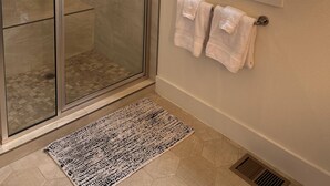 Ein Badezimmer mit Duschkabine, einem Fenster mit Jalousien und einem Handtuchhalter mit Handtüchern.