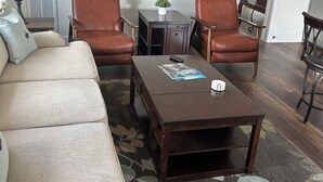Ein Wohnzimmer mit einer Couch, zwei Sesseln, einem Couchtisch, einem Beistelltisch mit Lampe und einer kleinen Pflanze.