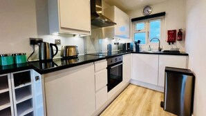 A modern kitchen with white cabinets, a stainless steel range hood, a built-in oven, and a black trash bin. - Luxury Scratby chalet with free swimming (Great Yarmouth)