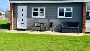 A residential building with a front door, two windows, a patio with chairs, and a bench. - Luxury Scratby chalet with free swimming (Great Yarmouth)