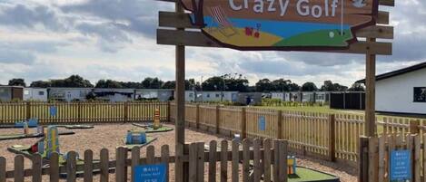 Señal de madera para Crazy Golf ASIS con un letrero de recepción de piscina debajo.