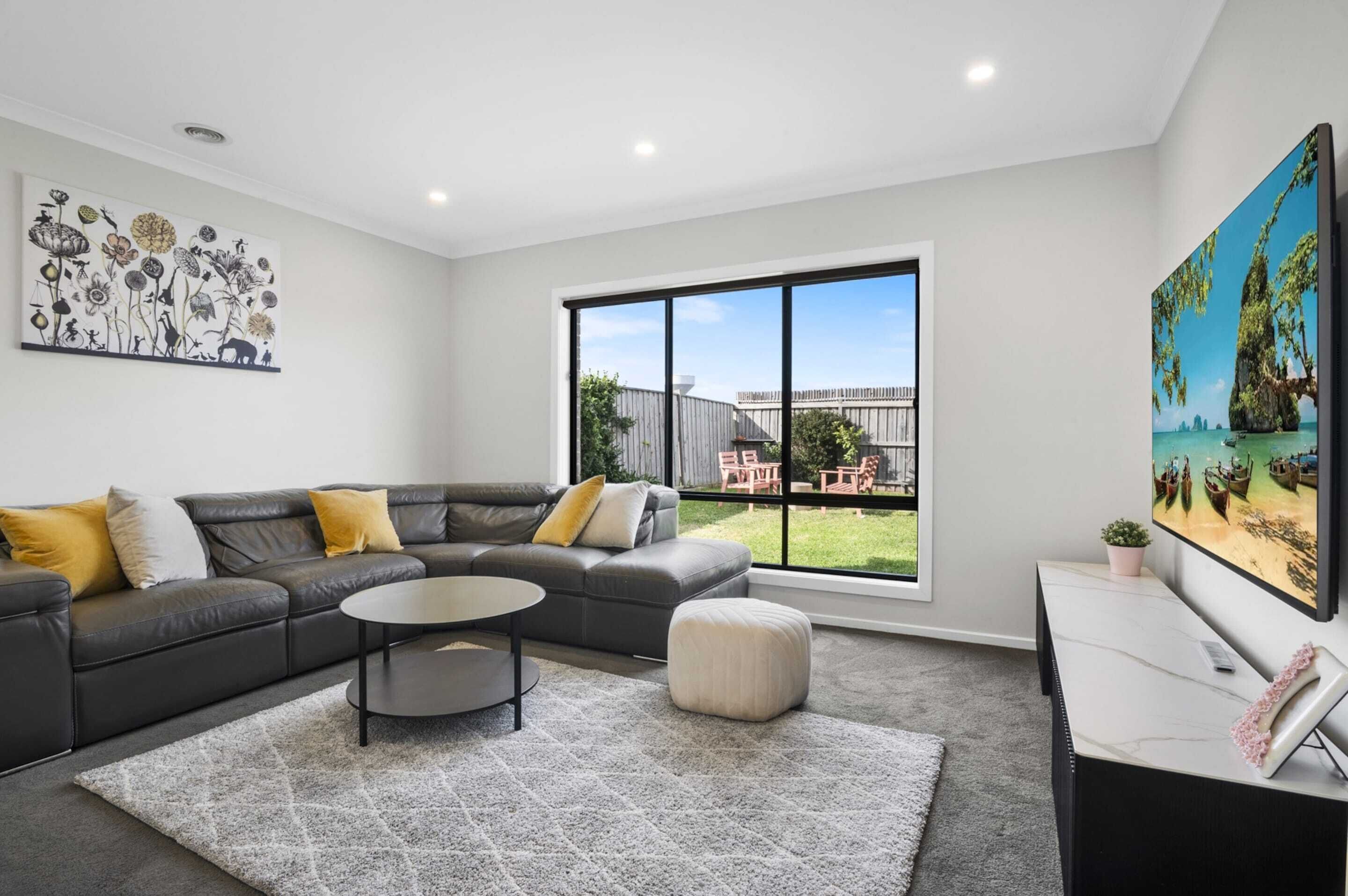 Un salón moderno con un sofá seccional gris, una mesa de centro redonda y un ventanal con vistas al exterior.