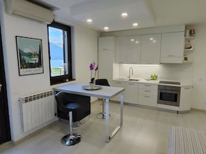 A modern kitchen with white cabinets, a stainless steel oven, a window with a view, and a bar stool. - Apartment "La Terrazza" Paratico (Paratico)