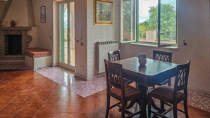 A dining area with a table and chairs, a fireplace, a window with a view, and a door leading outside.