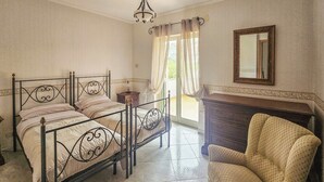 A bedroom with a four-poster bed, a wooden dresser, a chair, and a mirror on the wall.