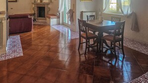 A spacious room with a fireplace, a dining table with chairs, and a red sofa.