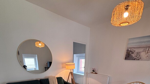 A living room with a dark green sofa, a round wooden coffee table with a plant, a wicker chair, a large mirror, and a hanging light fixture. - Ideal stay in Le Croisic (Le Croisic)