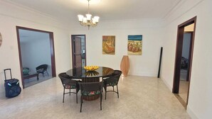 Un coin repas avec une table ronde, des chaises, un lustre, des œuvres d’art accrochées aux murs et une valise posée sur le sol.