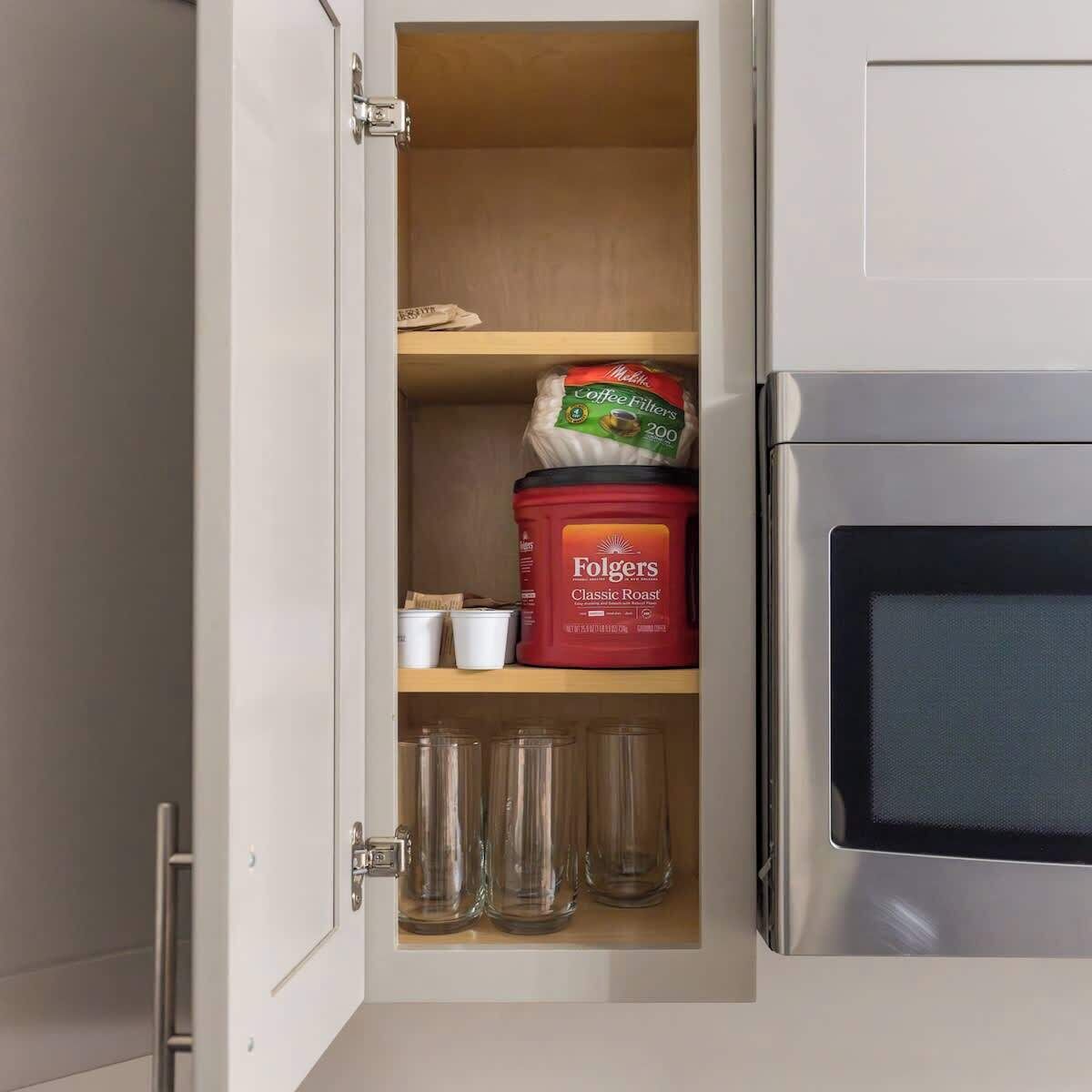 Un meuble de cuisine contenant une machine à café, un récipient pour les filtres à café et trois verres.