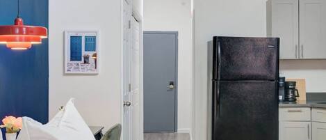 Une chambre d’hôtel compacte comprenant un lit, un mur d’accent bleu, une kitchenette avec un réfrigérateur et une porte donnant sur une autre pièce.