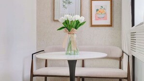 Une table ronde avec un pied noir, un banc recouvert d’un tissu beige et un vase contenant des fleurs blanches.