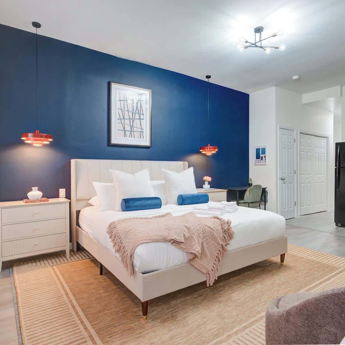 A modern bedroom with a large bed, bedside tables, a desk, and a wardrobe.