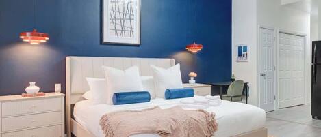 A modern bedroom with a large bed, bedside tables, a desk, and a wardrobe.
