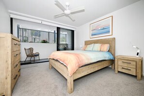 Une chambre à coucher comprenant un lit, une table de chevet, une commode, une chaise, un ventilateur de plafond et une fenêtre donnant sur un beau paysage.