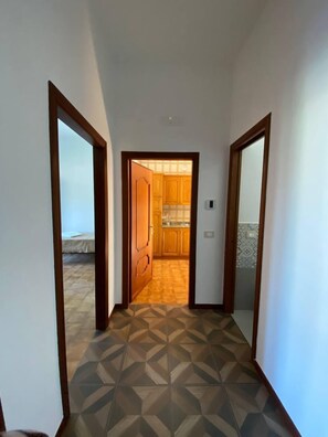 Ein Flur mit geometrisch gemustertem Bodenbelag, Holztüren und Blick in einen Küchenbereich.